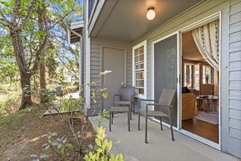 A patio with chairs and a table is on the front porch of a house. at Cedar Crest, Beaverton